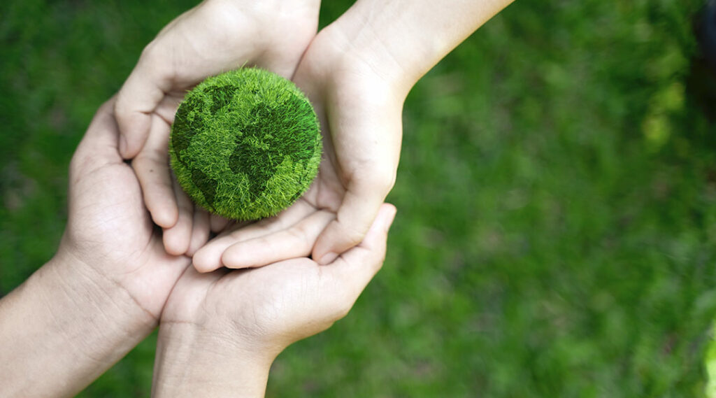 twee paar handen die een wereldbol gemaakt van gras vast hebben
