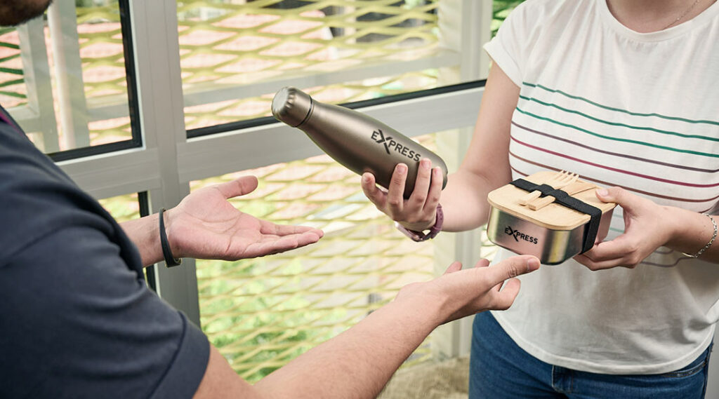 Iemand die een bedrukte drinkfles en broodtrommel met logo cadeau krijgt