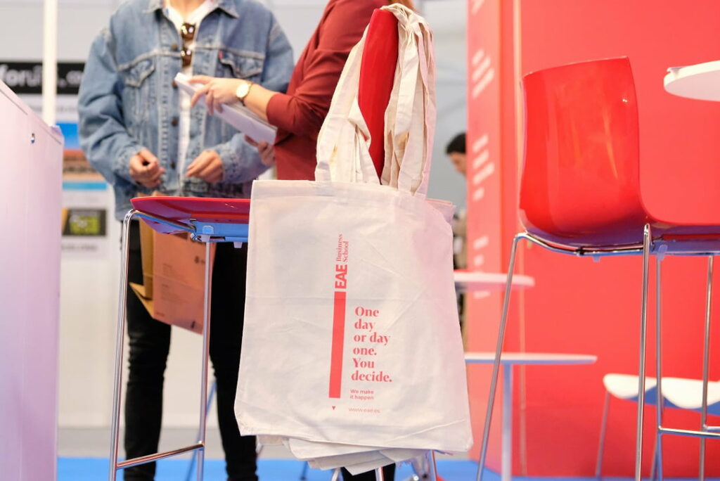 verschillende bedrukte tote bags die over een stoel hangen op een beurs